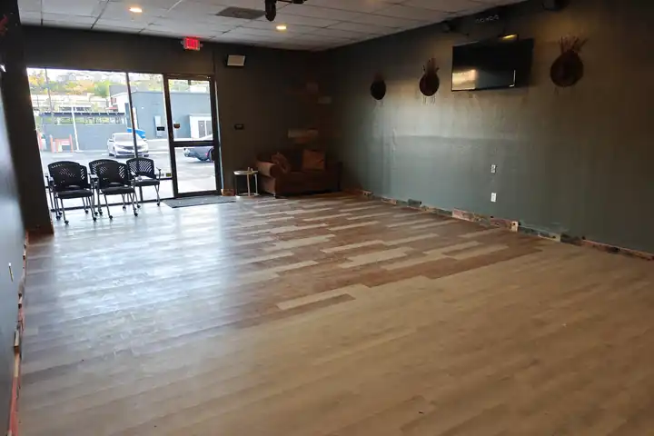 The Chopscape party room in daylight with an open wood floor, seating by the front window and a wall-mounted TV